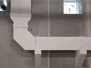 Weiß bekleideter Luftkanal, der an einer Betonwand entlang und durch eine Wandöffnung geführt wird